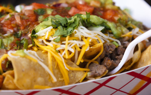 A close-up shot of a plate with delicious mexican style nachos with carne asada topped with guacamole and fresh salsa